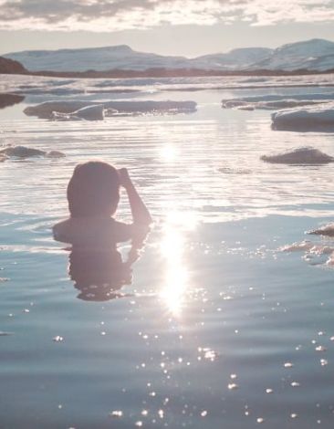 Girl taking an ice bath in a lake with ice in the sun.