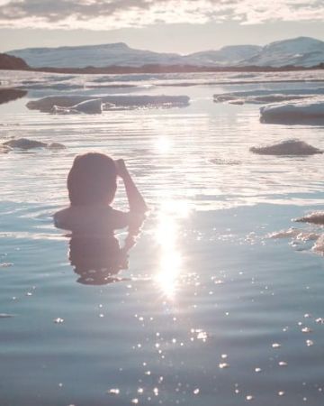 Girl taking an ice bath in a lake with ice in the sun.